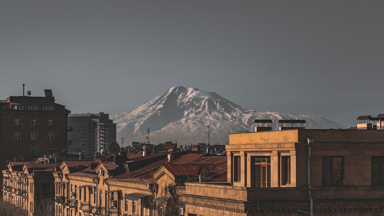 Երևանի տուֆե բնակելի շենքեր՝ կարմիր տանիքներով, իսկ նրանց հետևում՝ ձյունածածկ Արարատը