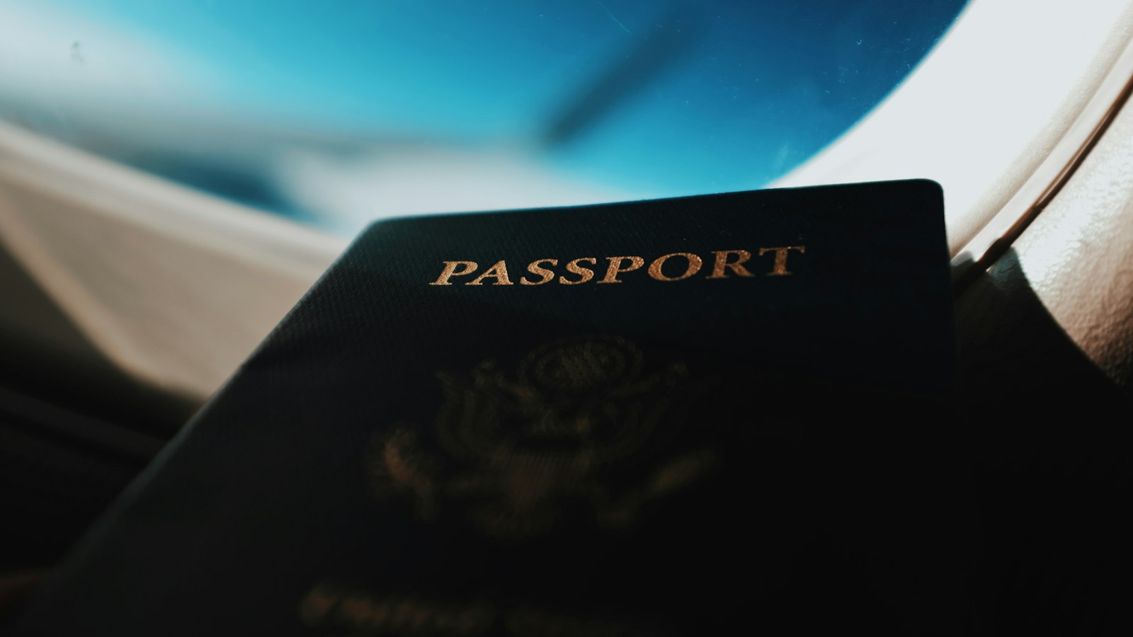 Dark outline of a passport held up against a bright airplane window and blue sky.