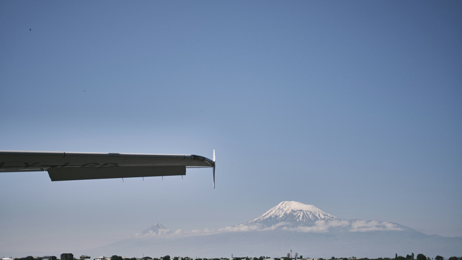 An aircraft wingtip at Yerevan airport with snow-capped Mount Ararat under a clear blue sky.